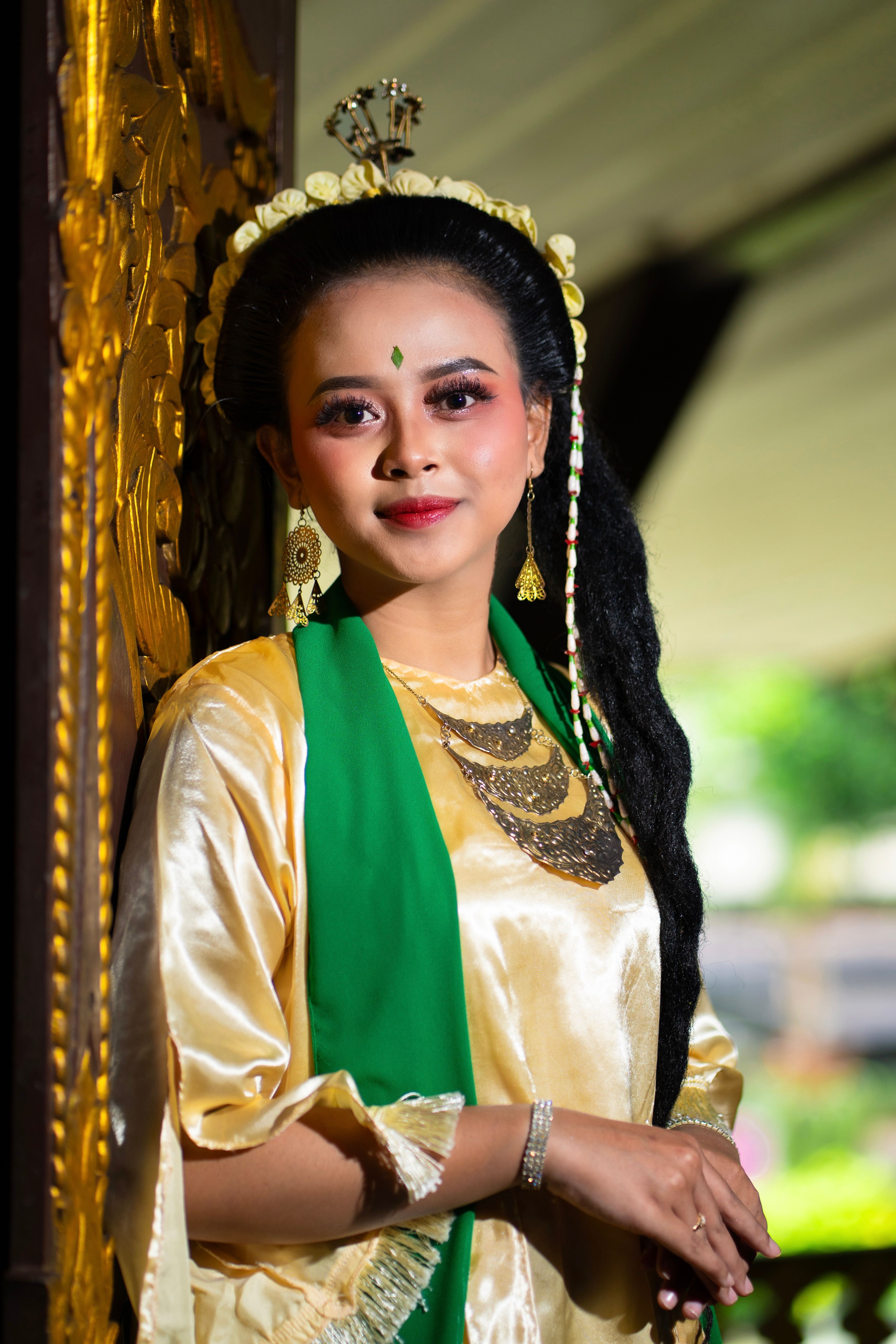 Woman in traditional Indonesian attire posing indoors with elegant accessories and makeup.