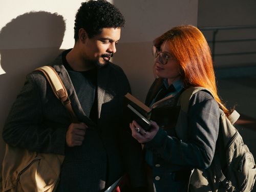 Free Two students engage in conversation while holding books in a dimly lit indoor setting in Buenos Aires. Stock Photo
