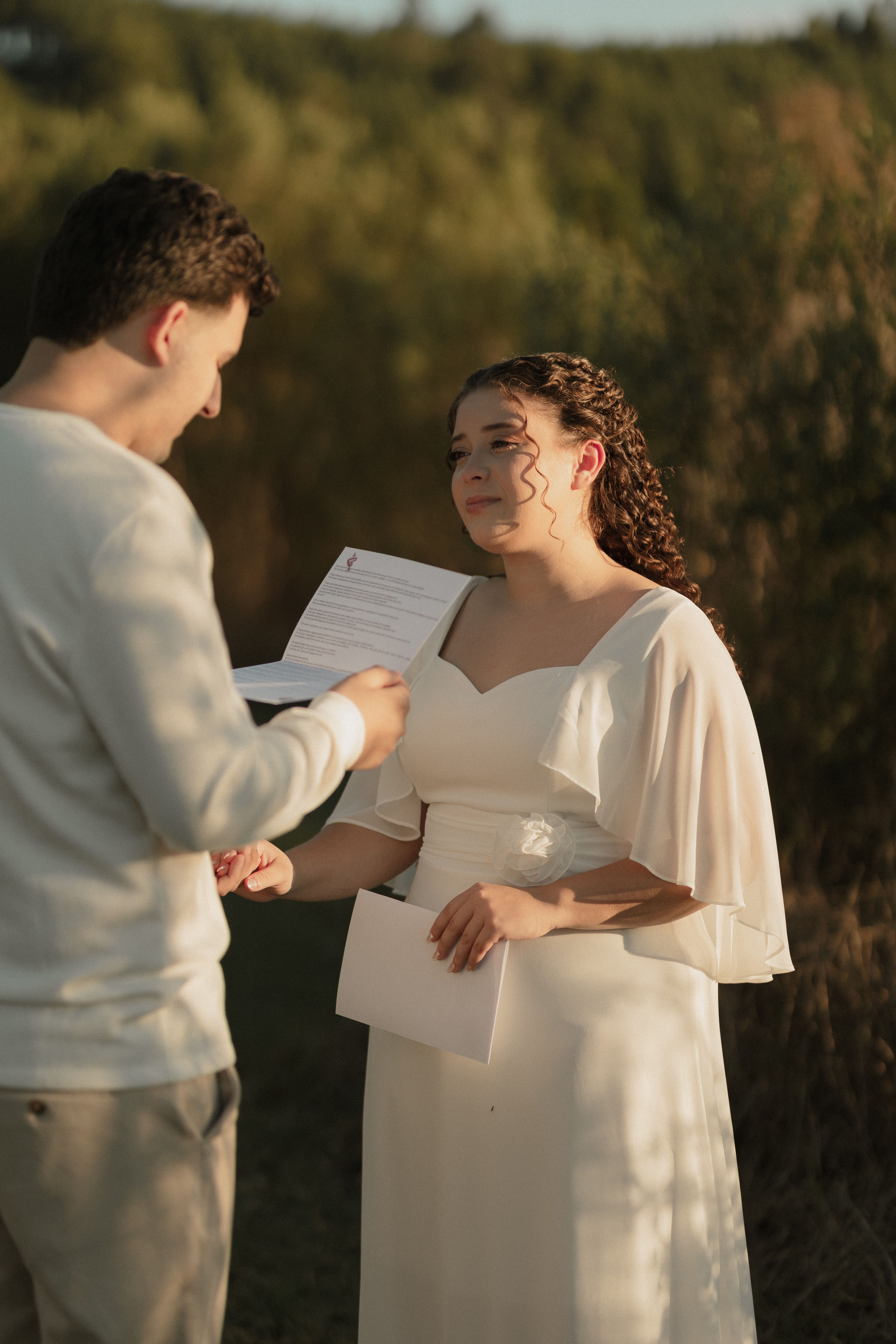 A bride and groom exchanging vows in a serene outdoor setting, captured during golden hour.