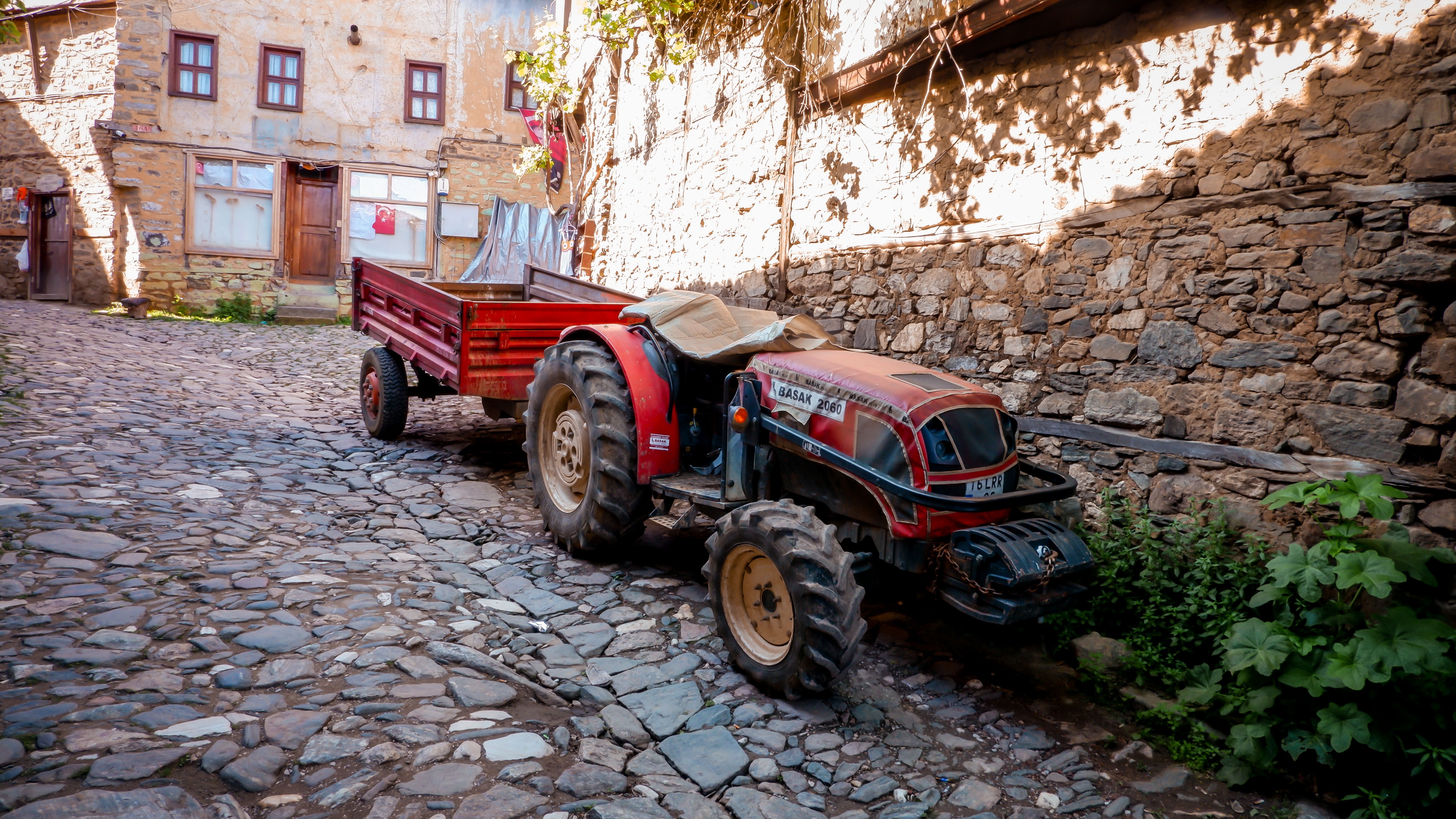 A red tractor parked on a cobblestone street in a quaint village setting.