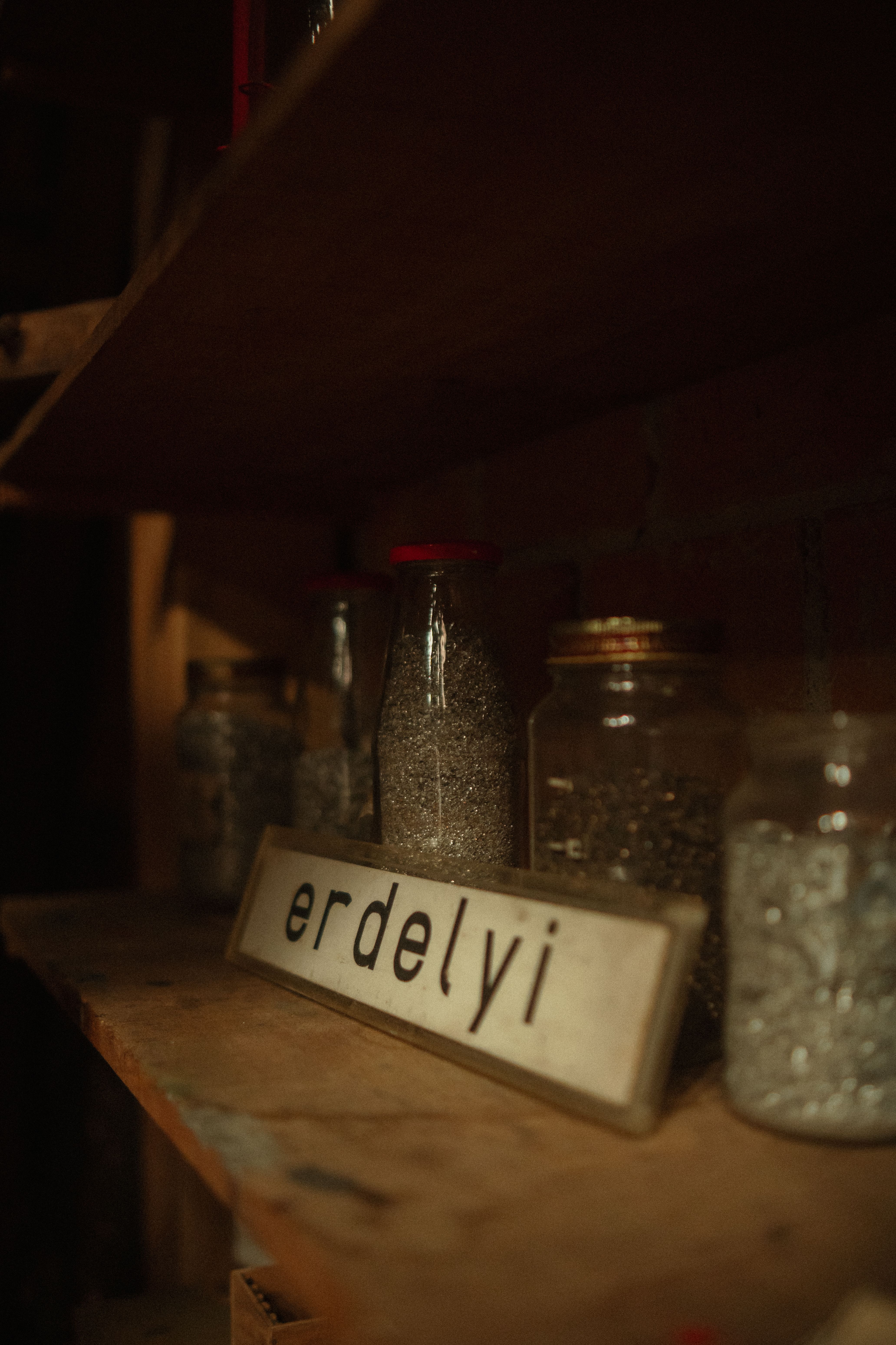A rustic shelf displays glass jars filled with metallic materials and a vintage Erdelyi sign.