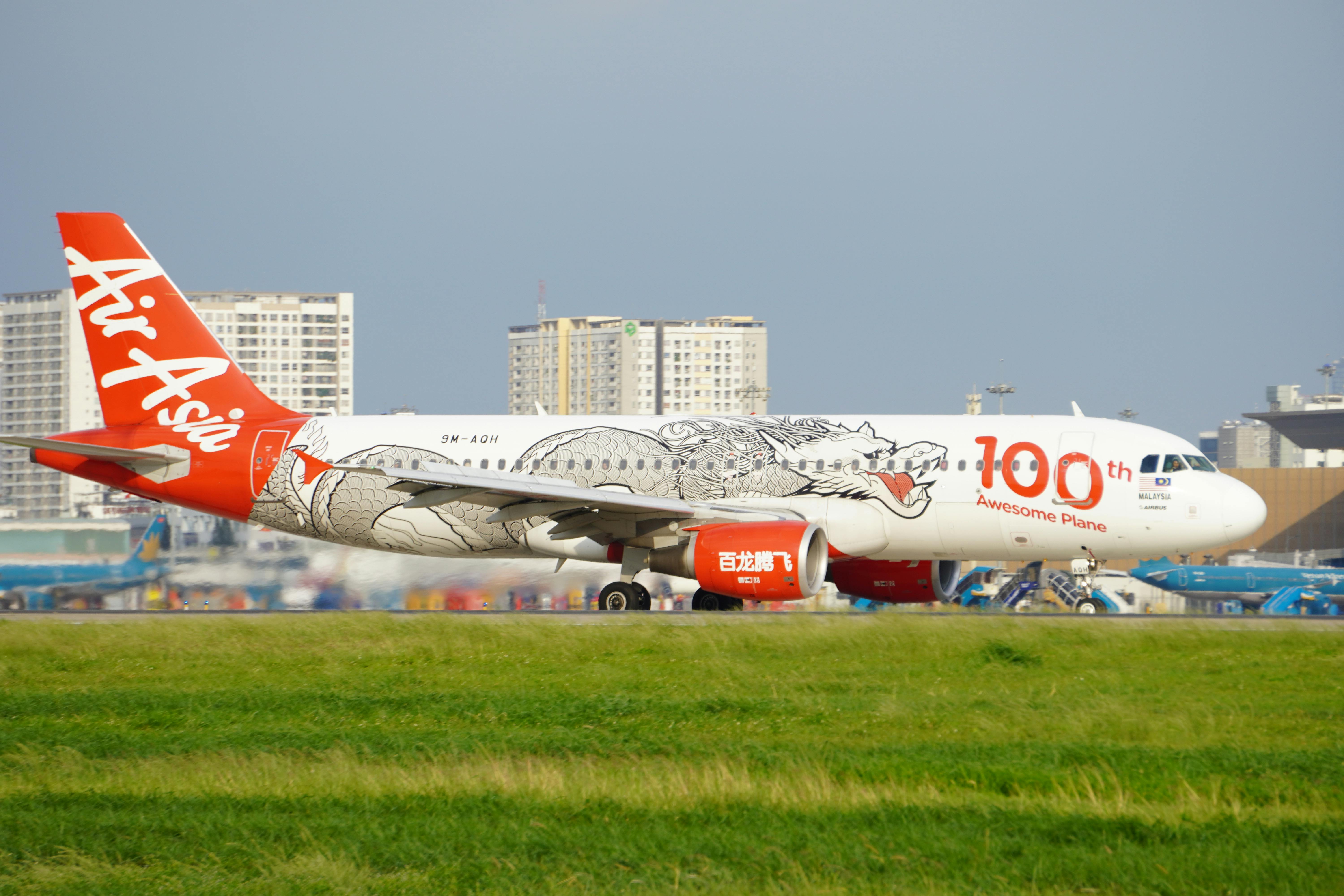 AirAsia Airbus A320 taxiing at airport with special dragon design livery celebrating 100th aircraft.