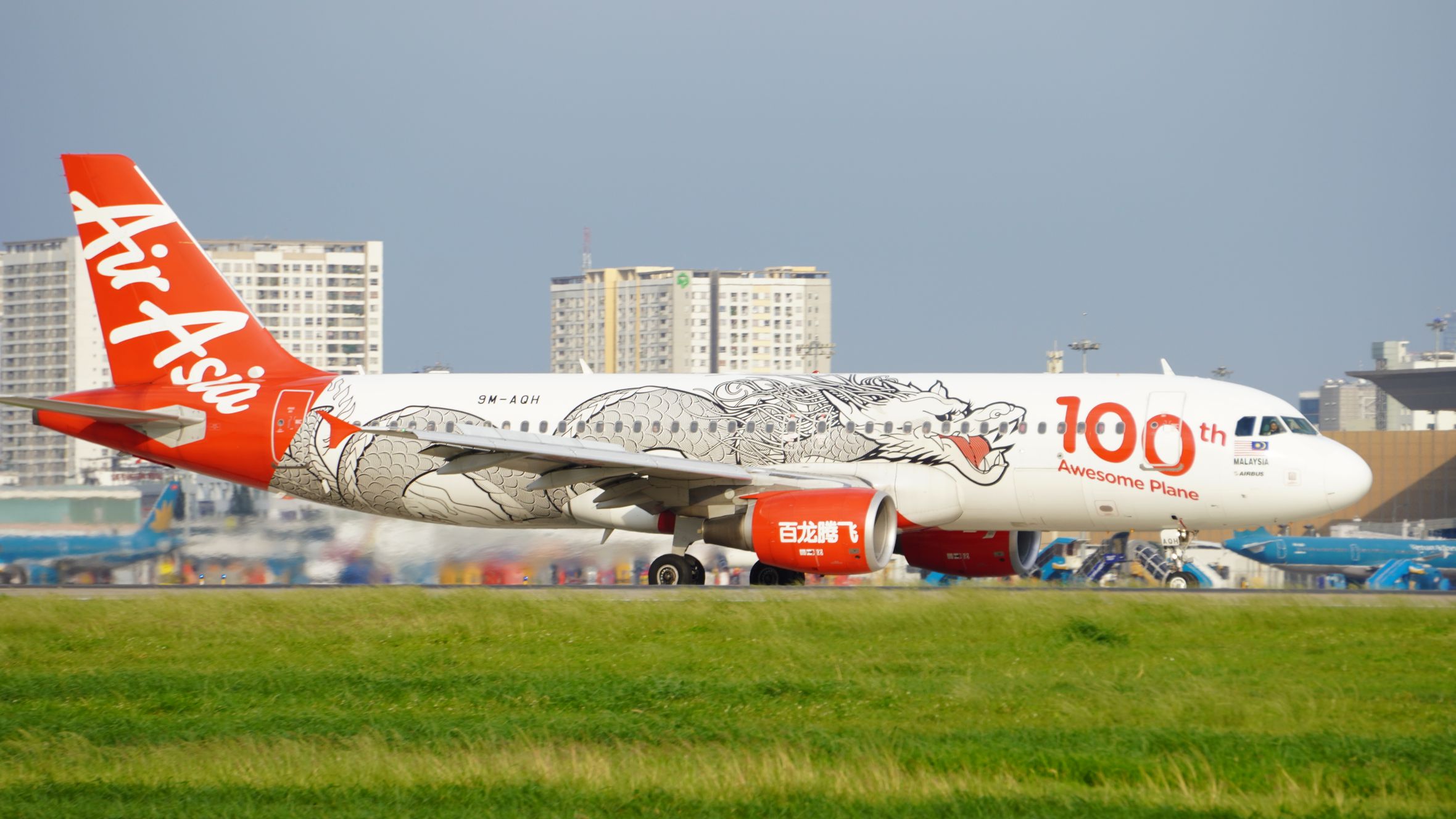 AirAsia Airbus A320 taxiing at airport with special dragon design livery celebrating 100th aircraft.