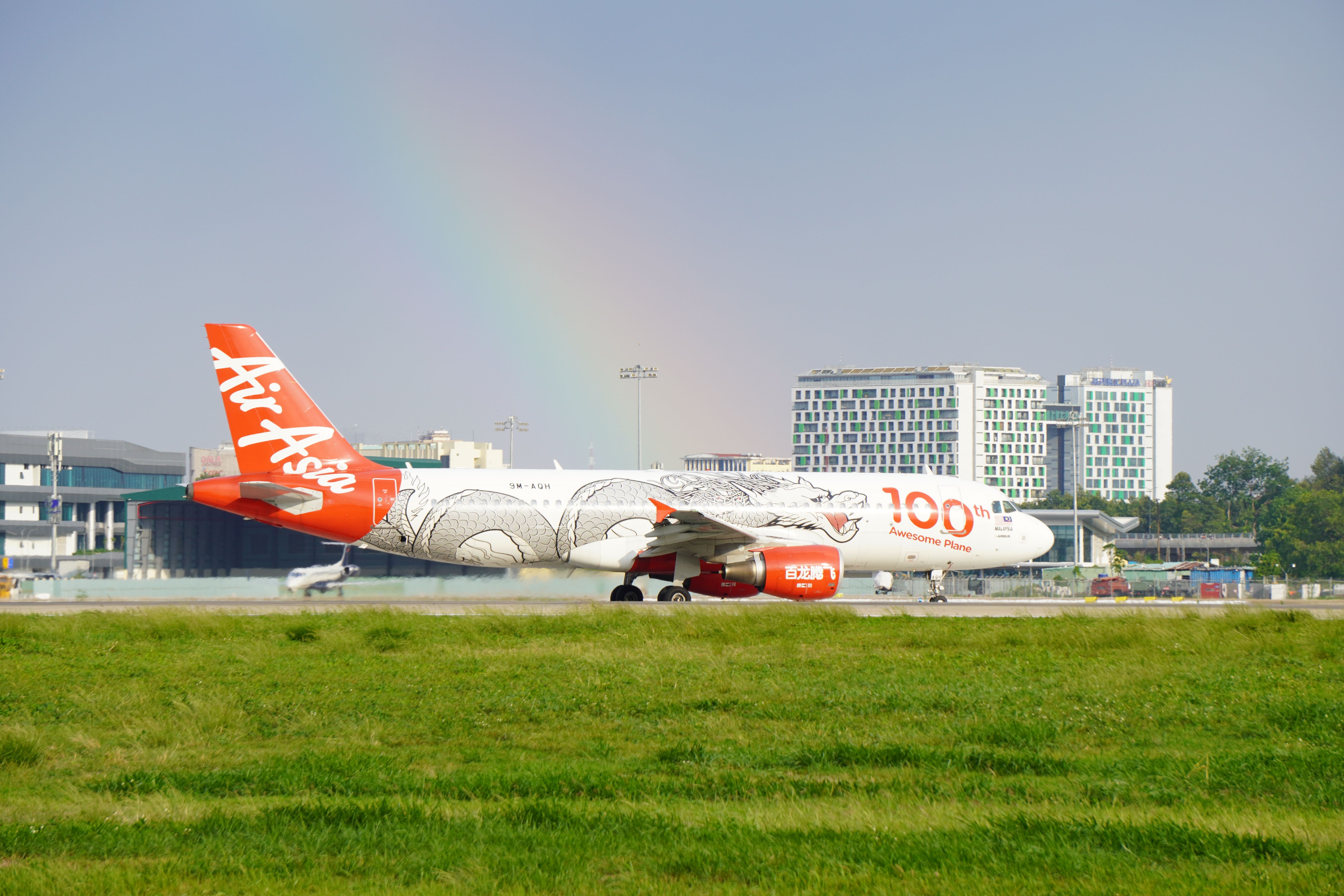 AirAsia aircraft on runway with rainbow and airport terminal in background.