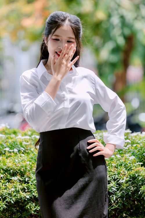 Free A young woman in formal attire laughing while standing in a sunny garden setting. Stock Photo