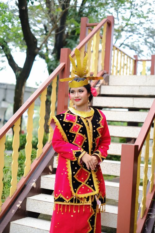 Free Woman in vibrant traditional Indonesian costume posing on outdoor staircase in Jakarta park. Stock Photo