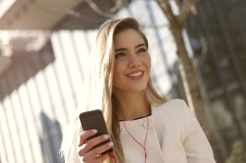 黒のスマートフォンを保持している白いブレザーの笑顔の女性