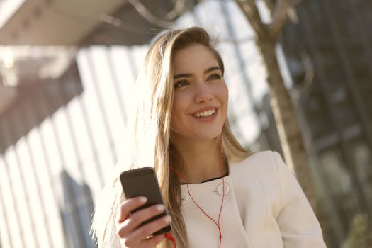 Cheerful woman in a white coat using smartphone outdoors with headphones.