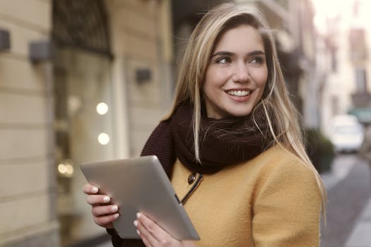 在城市环境中，一位穿着秋装的年轻女子拿着平板电脑微笑