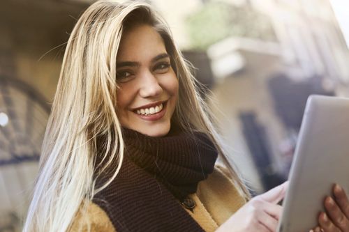 Free Smiling woman holding a tablet outdoors, captured in natural lighting. Ideal for technology and lifestyle themes. Stock Photo
