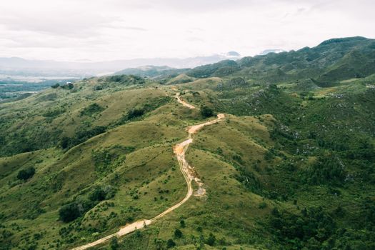 Breathtaking aerial view of a winding road through the lush green hills of Papua Pegunungan, Indonesia.