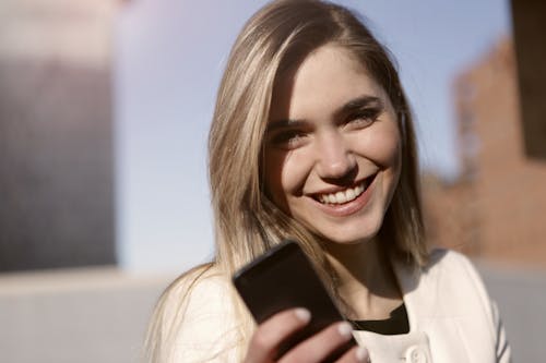 無料 黒のスマートフォンを保持している笑顔の女性 写真素材