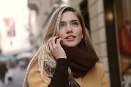 一位微笑着的女人，戴着围巾、穿着棕色外套，在户外抬头的特写镜头