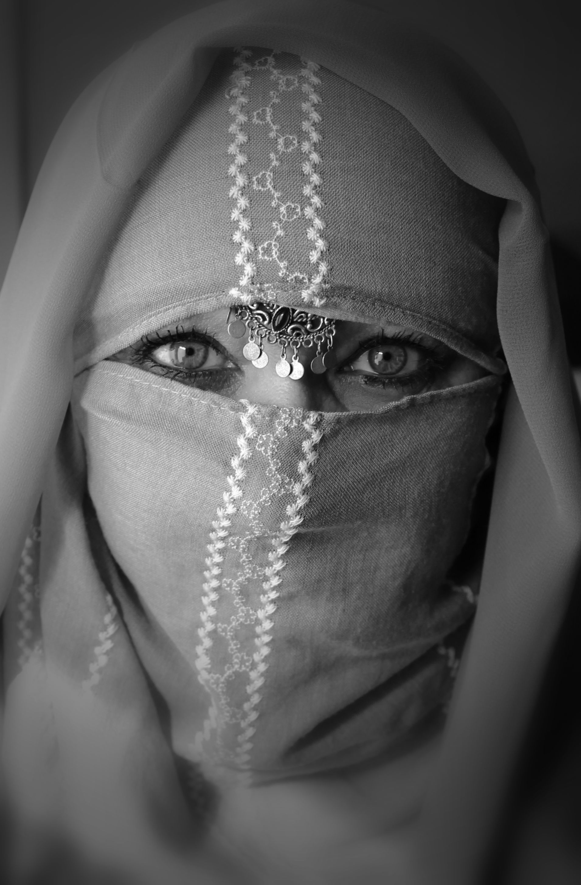 A captivating black and white portrait of a woman wearing a traditional veil adorned with intricate jewelry.