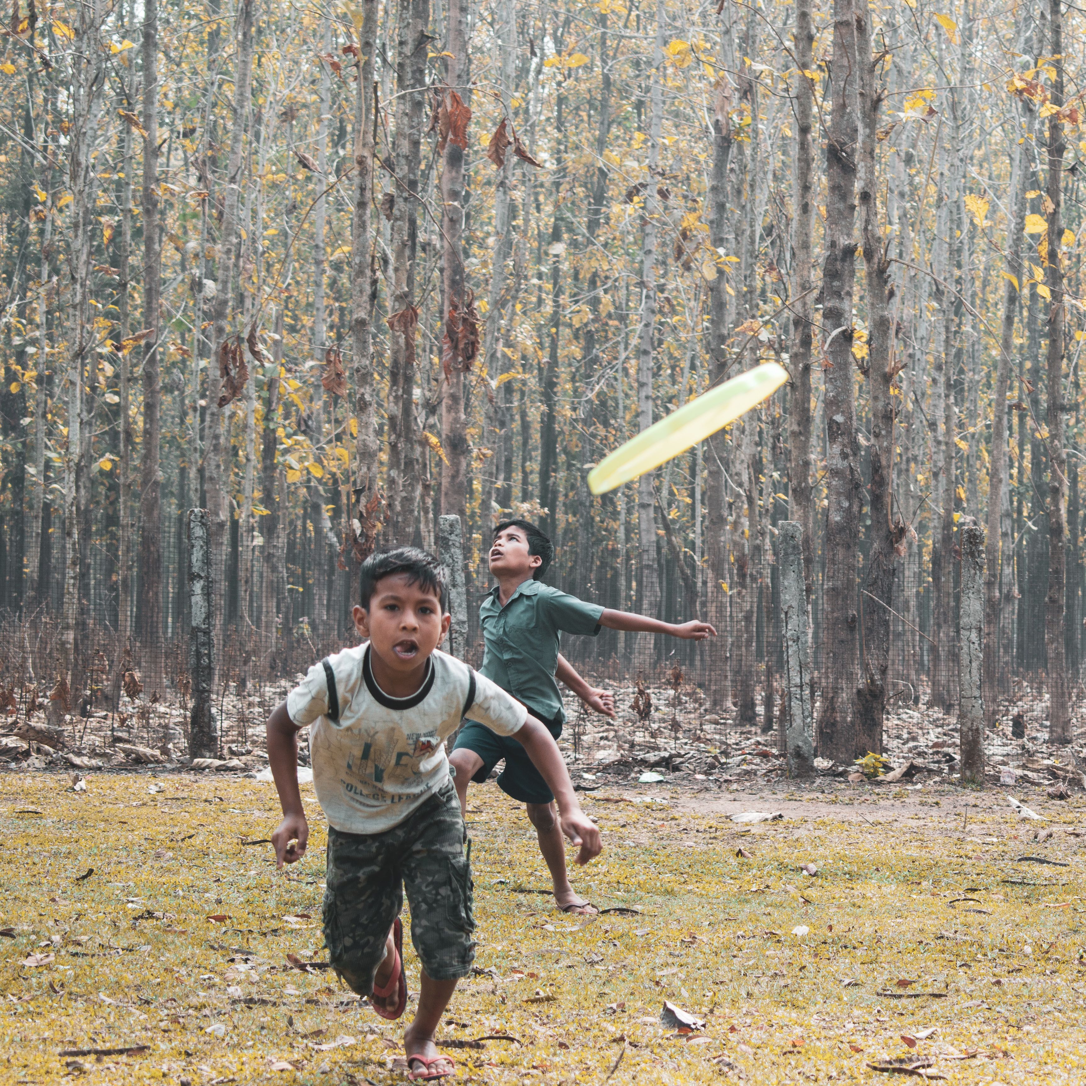 Two boys playing frisbee in an Assam forest, enjoying outdoor fun and nature.
