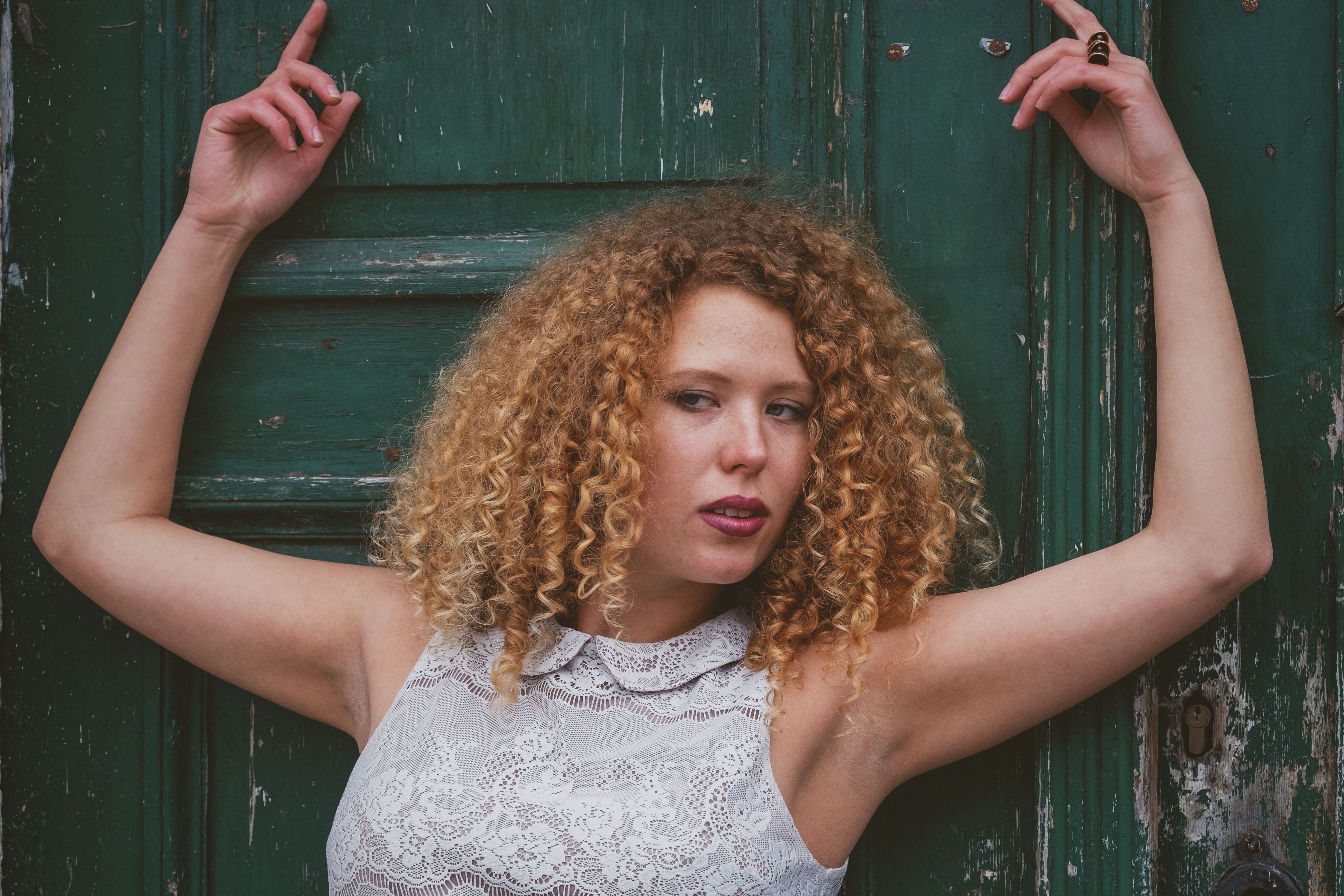 Stylish woman with curly hair poses against a vintage green door.