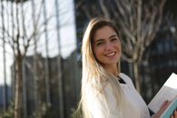 一位金发微笑的年轻女子拿着一本书站在户外，画面捕捉到了充满活力、令人振奋的瞬间