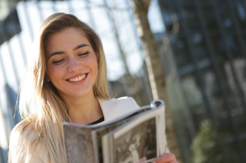 Free A joyful woman with blond hair reading a magazine outdoors with a sunny backdrop. Stock Photo