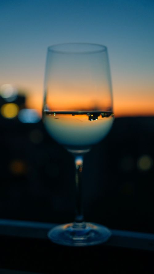 Free A wine glass reflecting a cityscape during sunset, creating a serene ambiance. Stock Photo