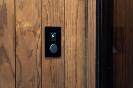 Close-up of a modern sauna control panel featuring a digital thermostat on a wooden wall, highlighting Scandinavian design.