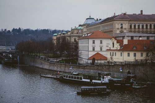 Free View of Prague's historic riverside with boats, classic architecture, and a tranquil river scene. Stock Photo