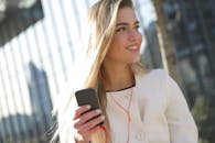 一位女士戴着耳机，在城市户外微笑着使用智能手机