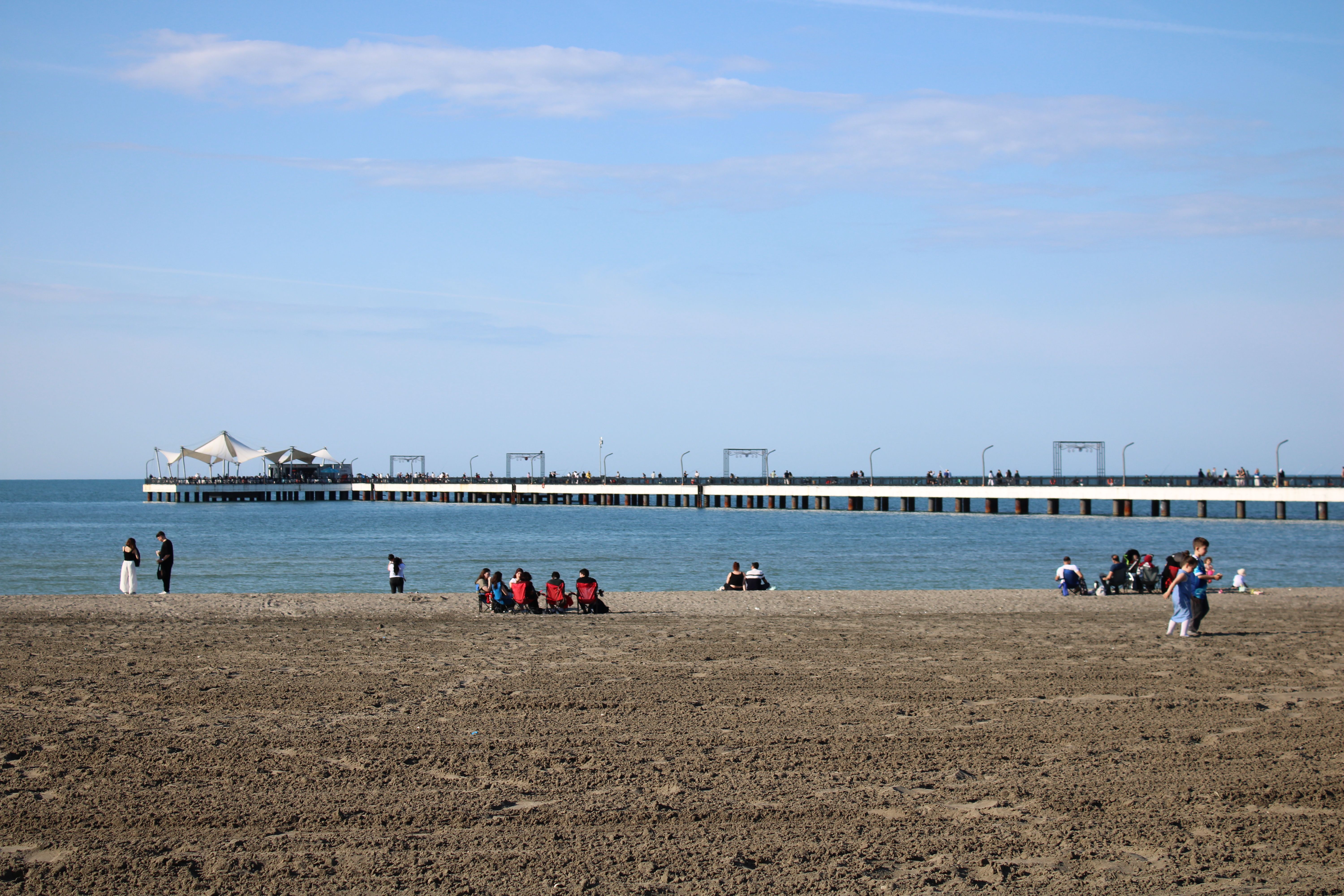 People relaxing on the Samsun beach with a scenic pier stretching into the sea under a clear blue sky.