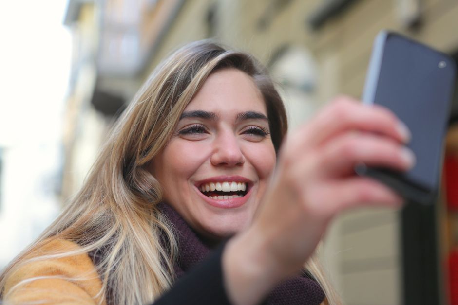 Young woman smiling while taking a selfie outside with a smartphone.
