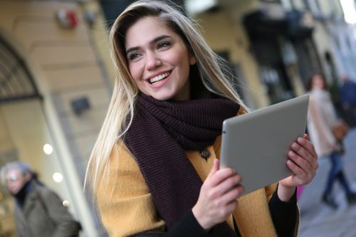 Free A cheerful woman with a tablet in an urban setting, highlighting modern mobile technology. Stock Photo