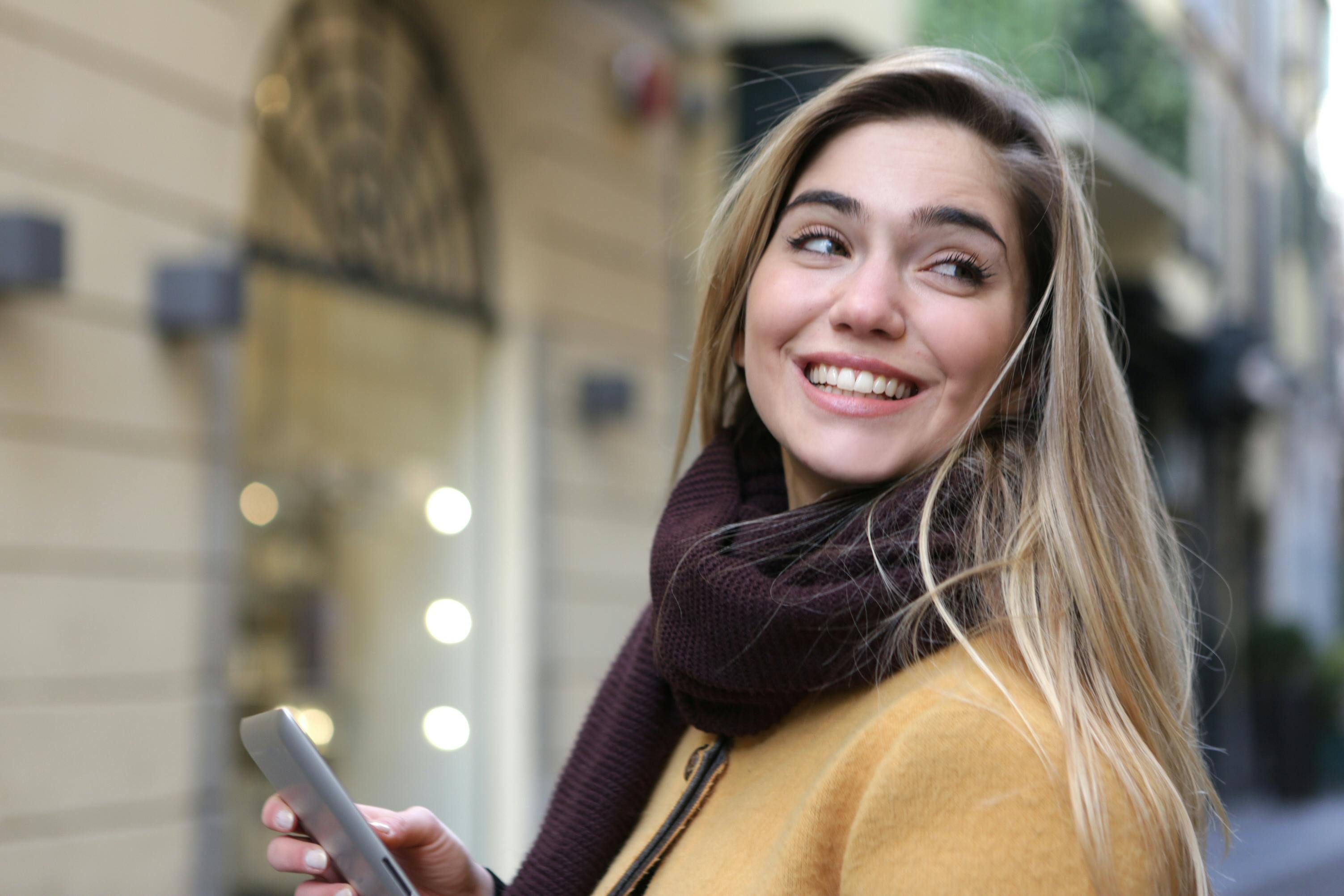 一位金发、戴着智能手机的快乐年轻女子正在享受户外生活
