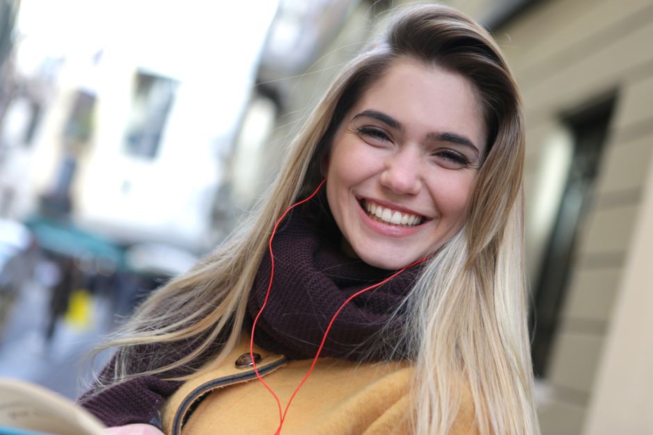A joyful young woman with headphones enjoying music in an urban setting.