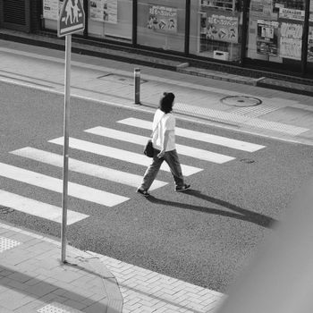 A silhouetted individual crosses a zebra crossing in a cityscape.