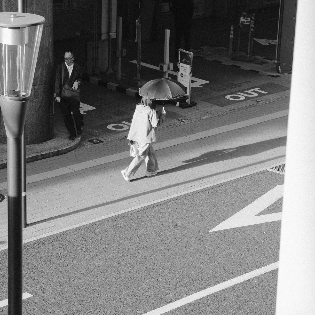 Black and white street scene captures a person with an umbrella, creating a striking shadow.