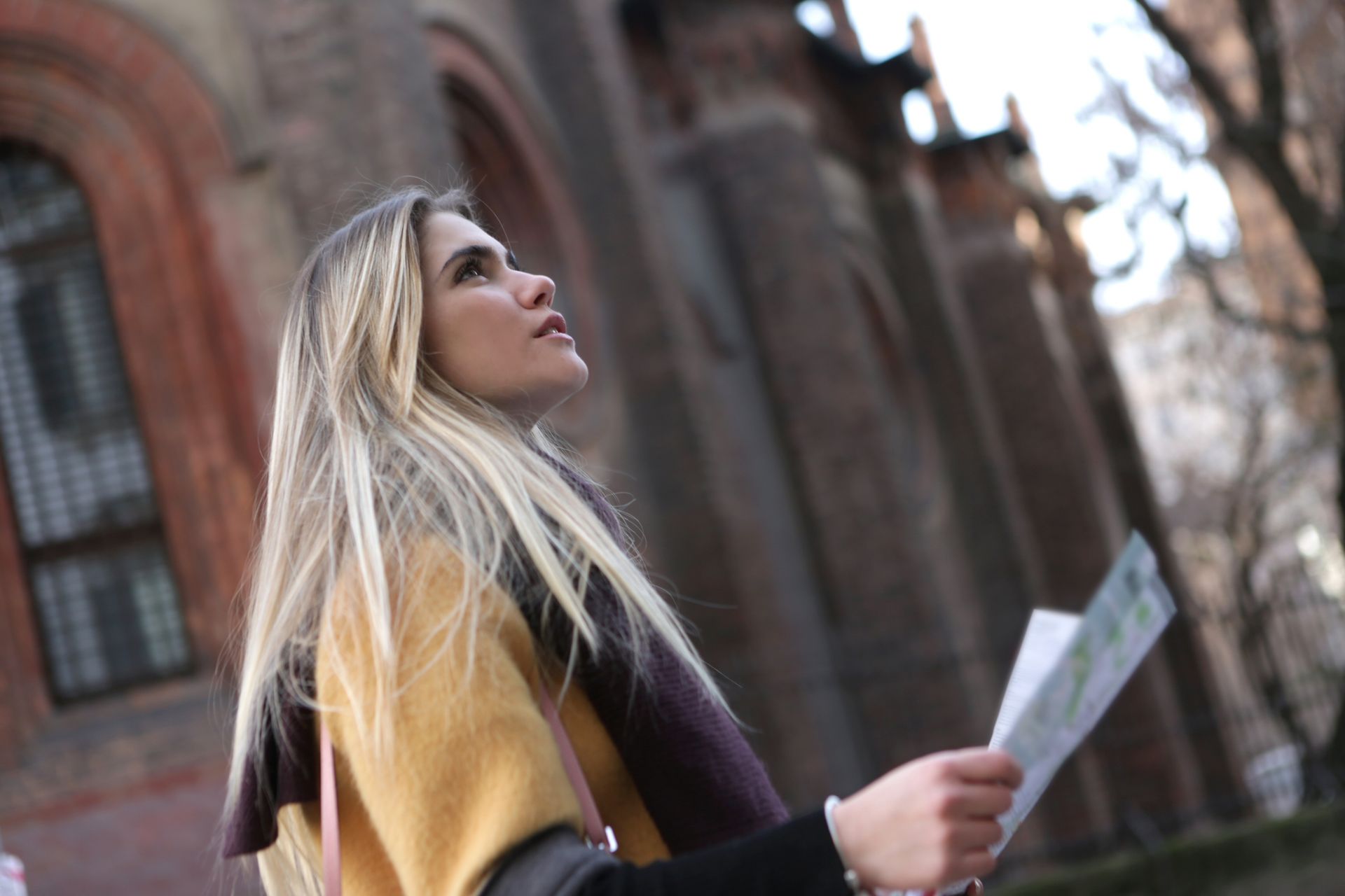 A young woman with long hair looks up while holding a map in an urban setting.