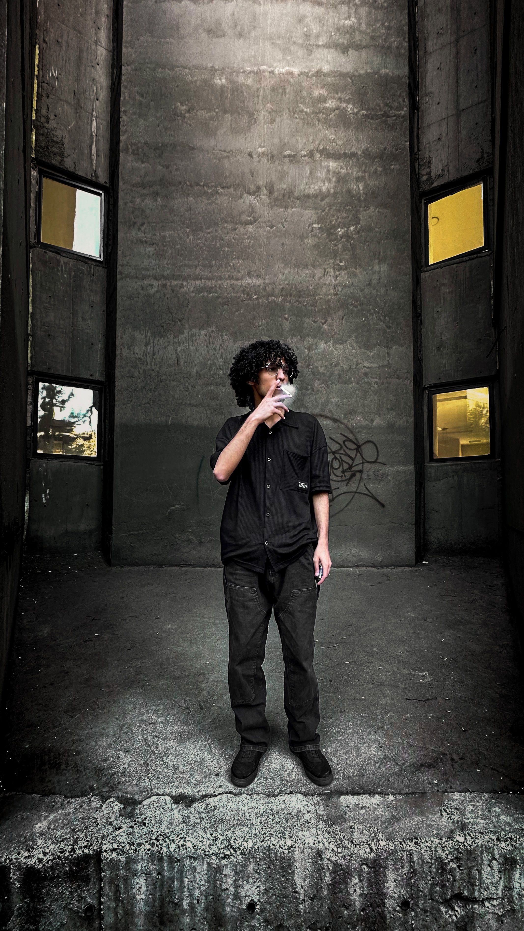 Young man smoking in a gritty urban alleyway with concrete walls and dim lighting.