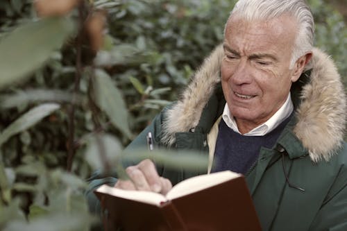 Free Man in Green Coat Writing On The Book Stock Photo