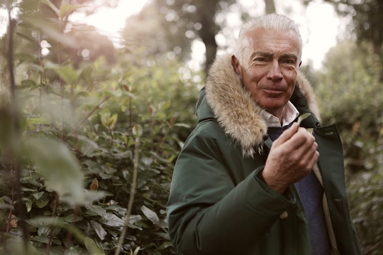 Man In Green Parka Jacket Standing Near Green Plants