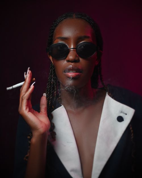Free Dramatic portrait of a stylish woman in sunglasses smoking in a moody dark environment. Stock Photo