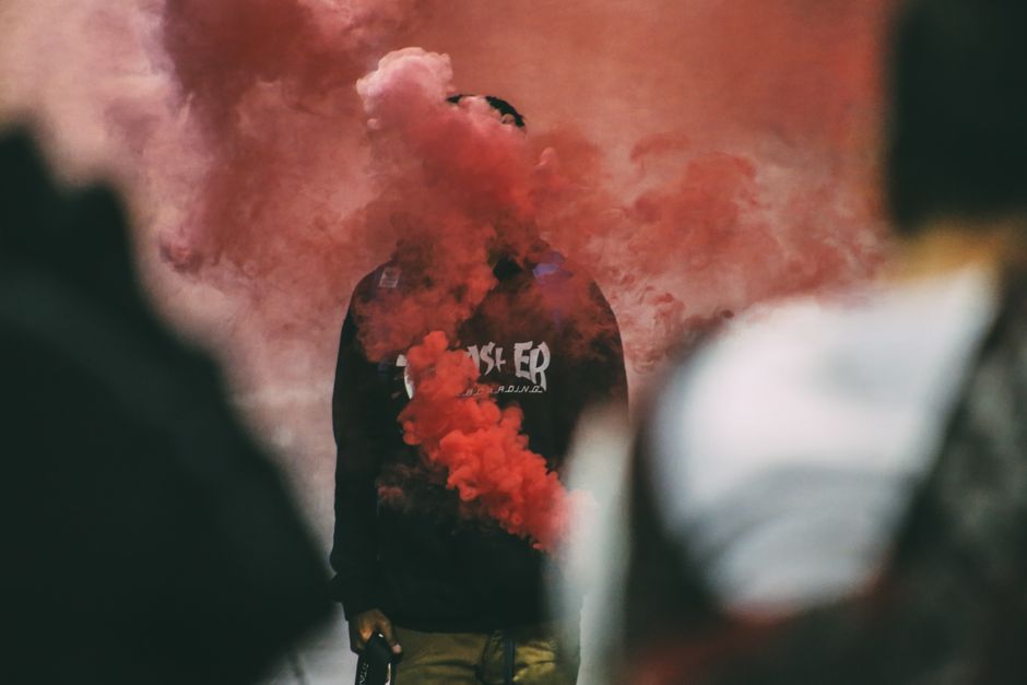 A person in a hoodie obscured by vibrant red smoke creating a dramatic effect.
