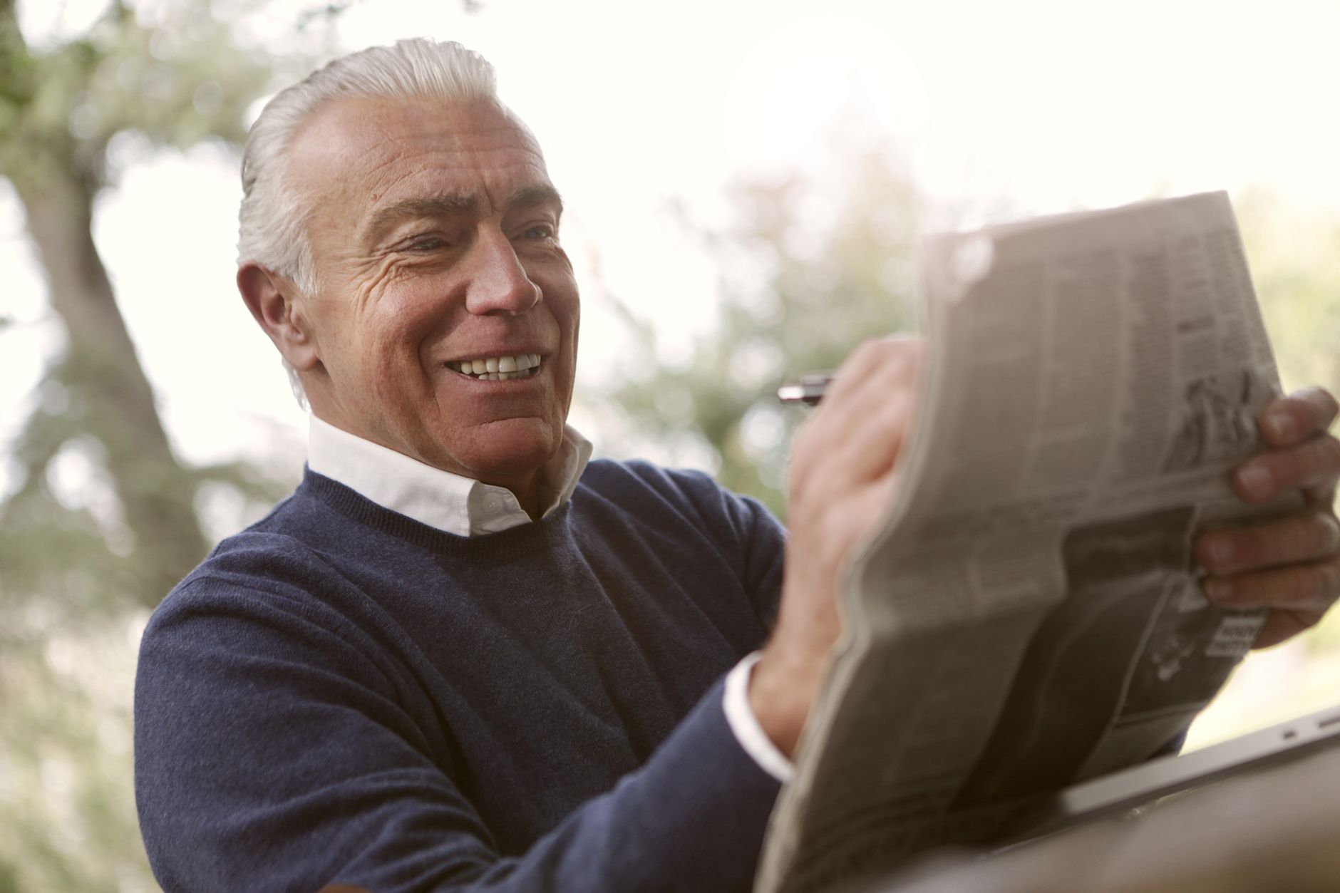 A happy senior man reading a newspaper outdoors, enjoying a sunny day.