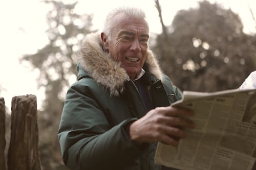 Man In Green Jacket Holding A Newspaper