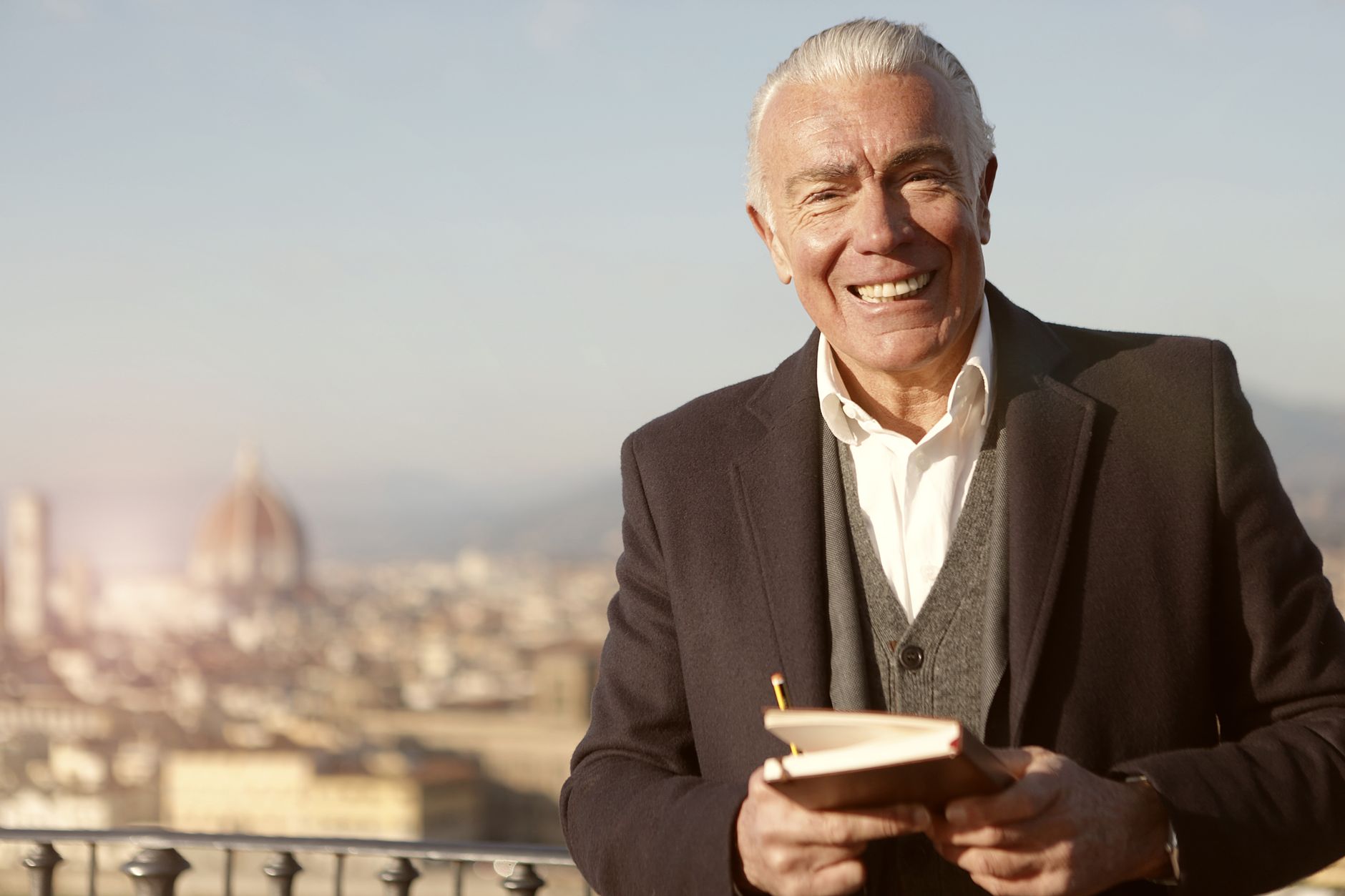Senior man smiling with a notebook overlooking Florence skyline. An expression of joy and wisdom.