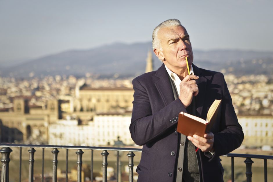 Thoughtful man with an open notebook overlooks a European cityscape, capturing a moment of reflection.