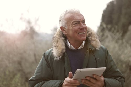 Man in Green Jacket Holding Silver Ipad