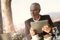 咖啡馆外，一位老人坐在那儿，用着平板电脑，表情若有所思