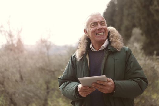 Happy senior man in winter coat enjoying a day outdoors with a tablet.