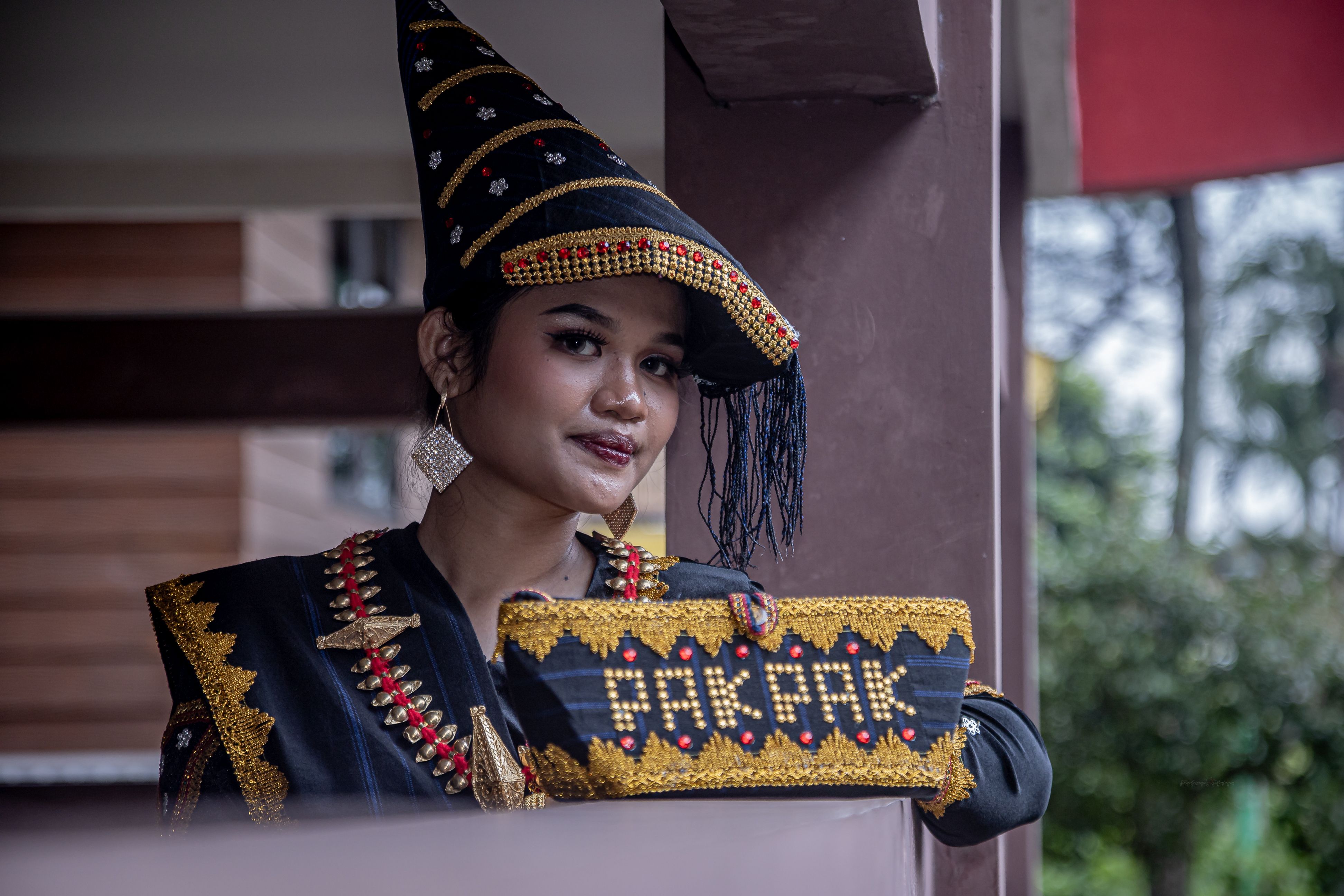 A woman in traditional Batak attire poses indoors in Jakarta, showcasing Indonesian culture.
