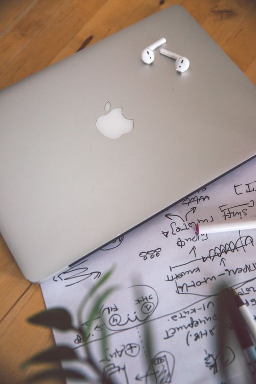 Free Minimalist workspace featuring a laptop, earbuds, and handwritten notes for planning and productivity. Stock Photo