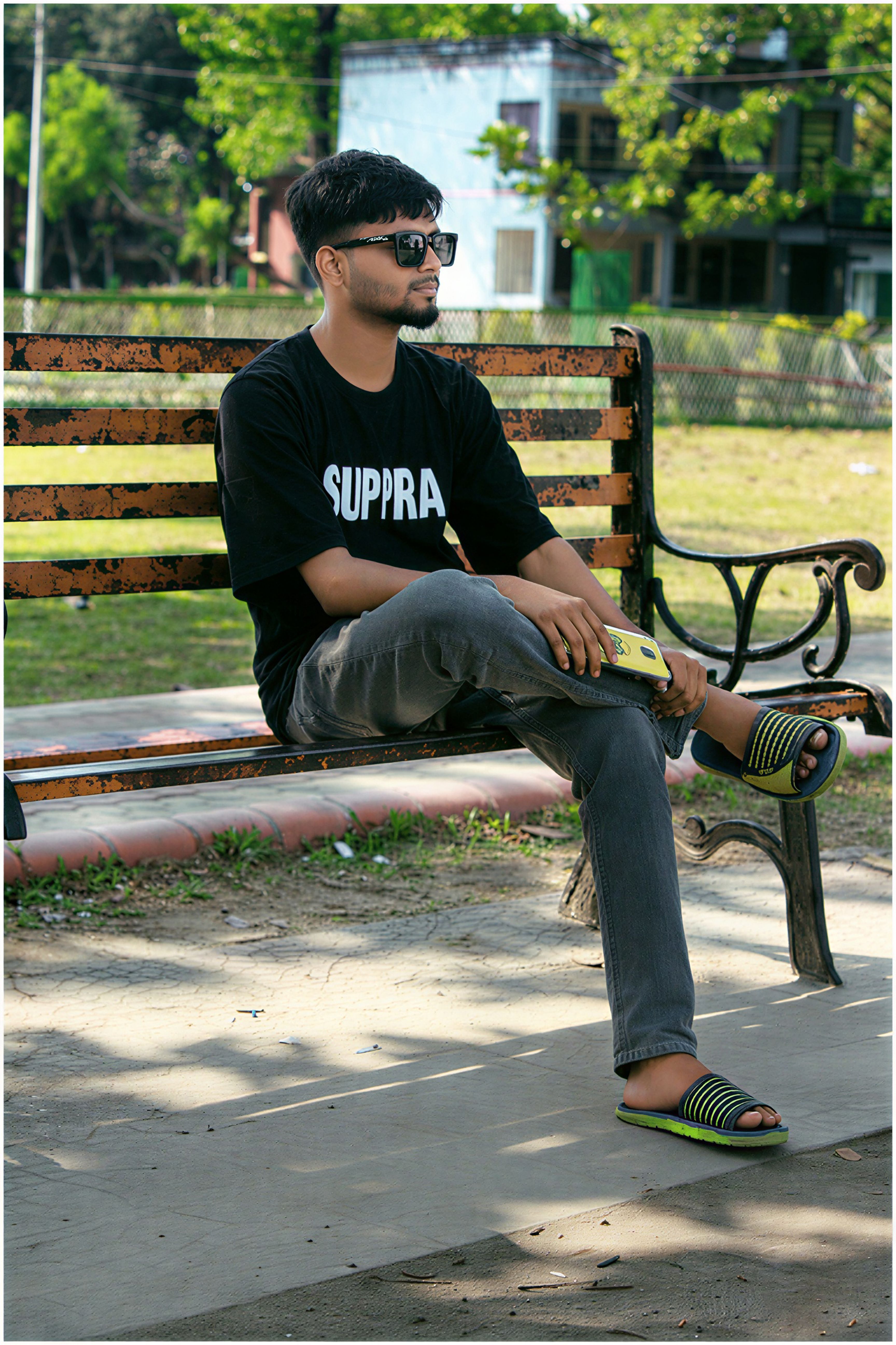 A young man sitting on a park bench in Rangpur Division, Bangladesh, enjoying a sunny day.