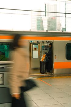 A bustling train station scene with a blurred pedestrian and an open train door, depicting urban transportation.
